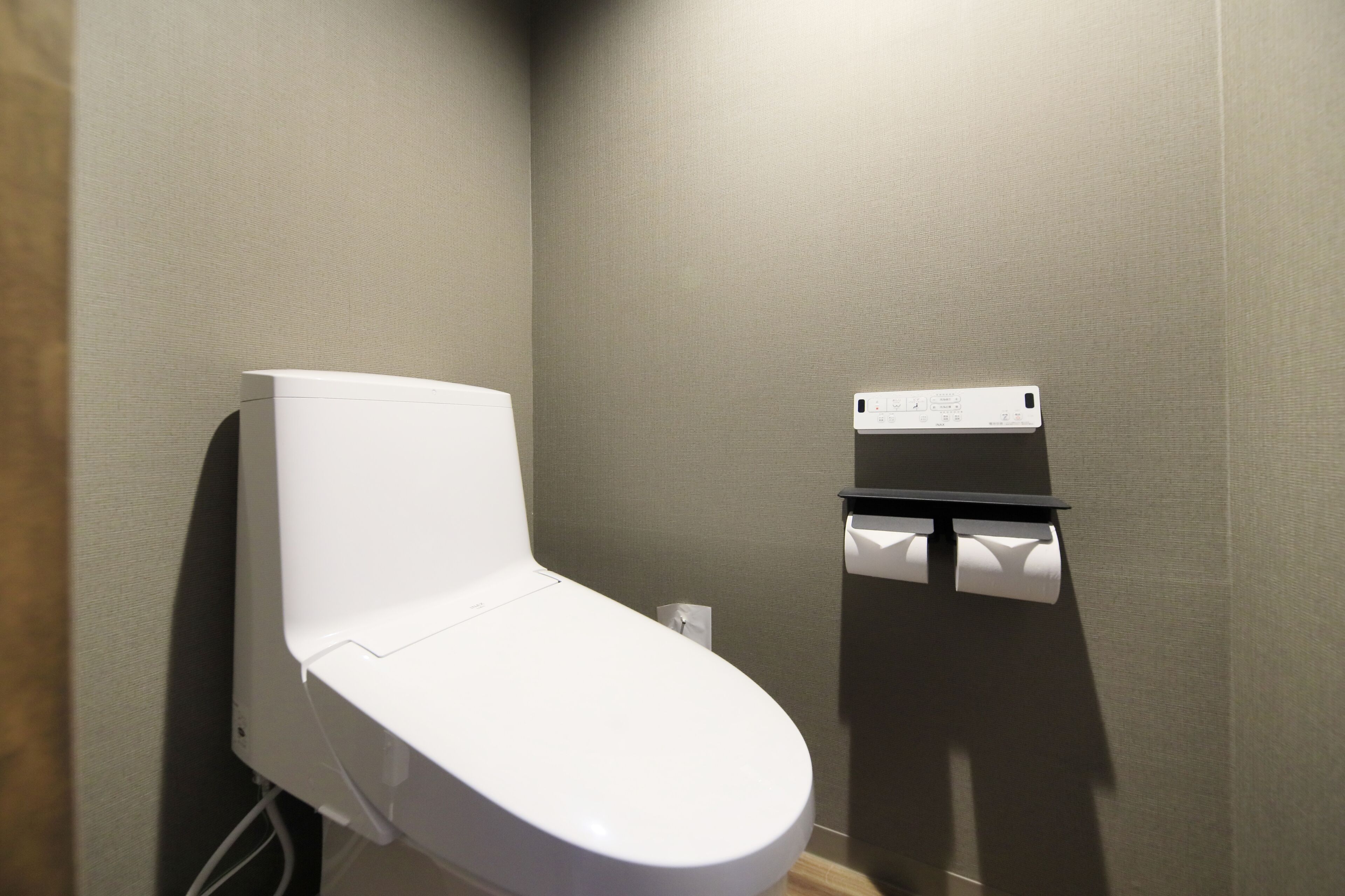 Une salle de bain moderne avec des toilettes blanches, un distributeur d’essuie-tout et une prise électrique murale.