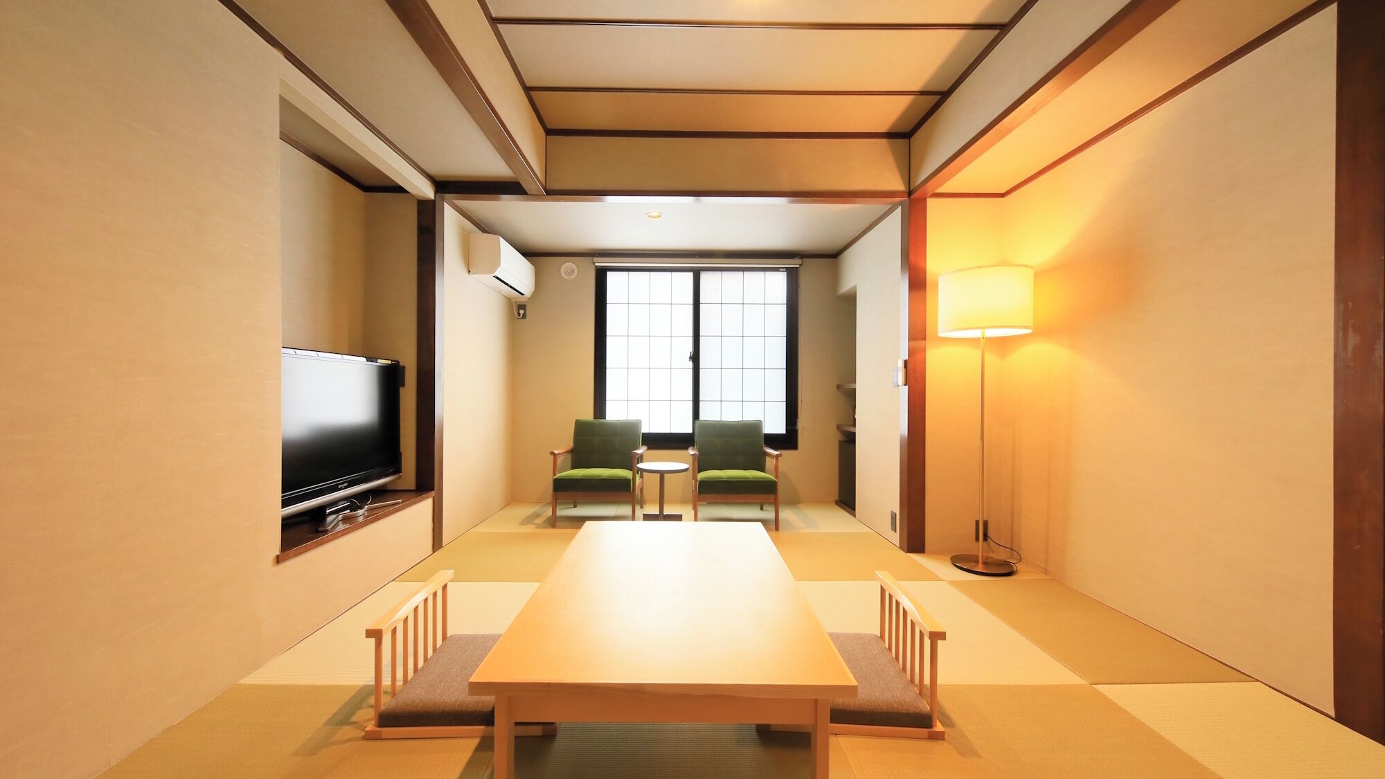 Une chambre d’hôtel équipée d’une télévision, d’une table en bois, de deux chaises, d’une petite table et d’un lampadaire.