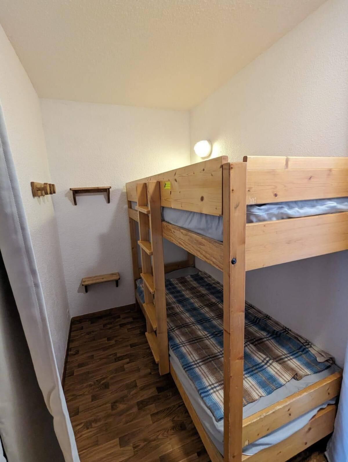 Een slaapkamer met stapelbedden, een houten vloer, een klein plankje en een wandlamp.