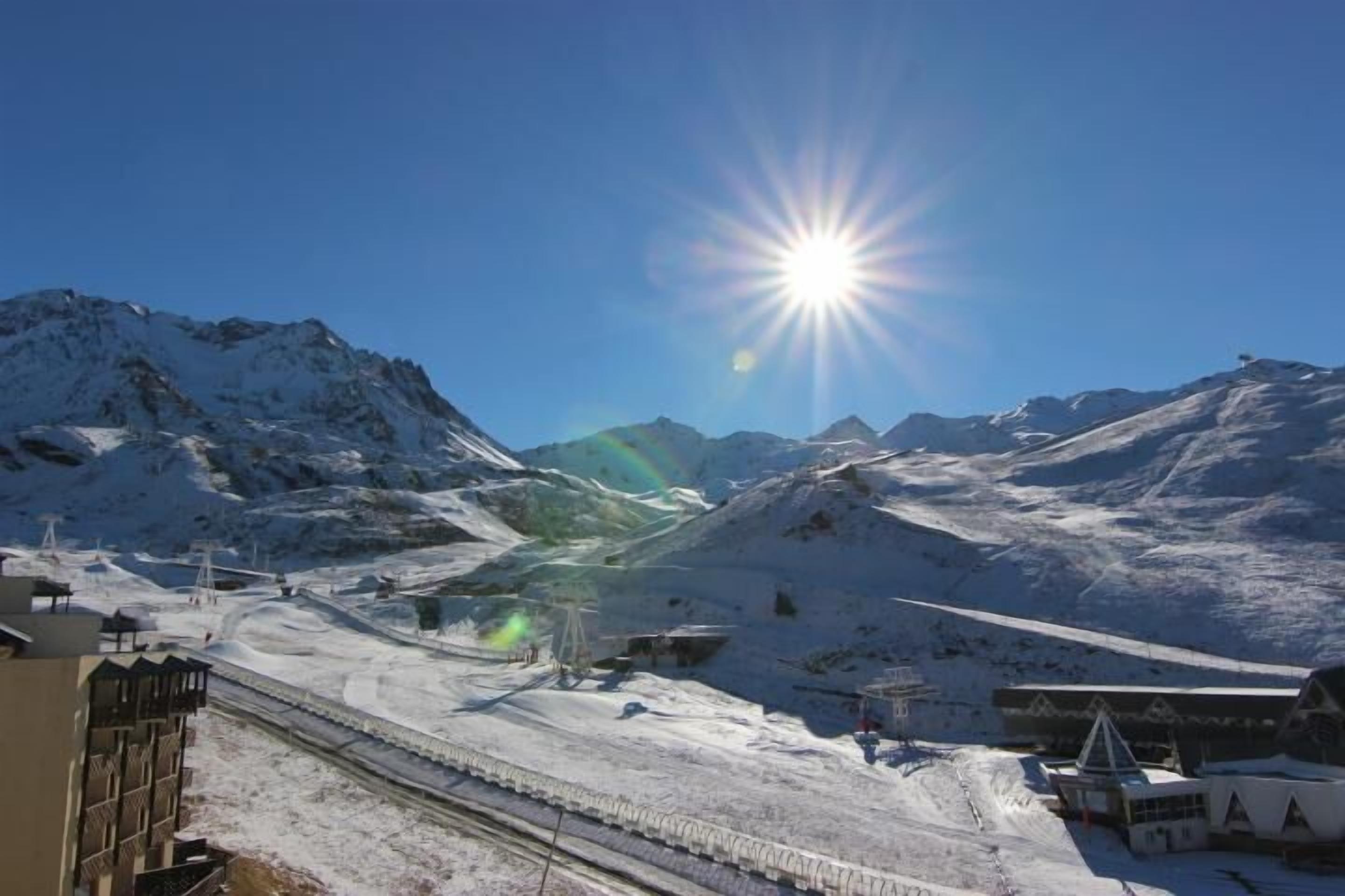A snowy mountain landscape with a clear sky and a bright sun.