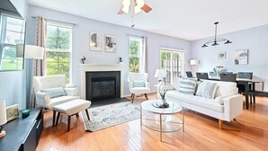 Ett rymligt vardagsrum med en öppen spis, vita soffor och en matplats.
