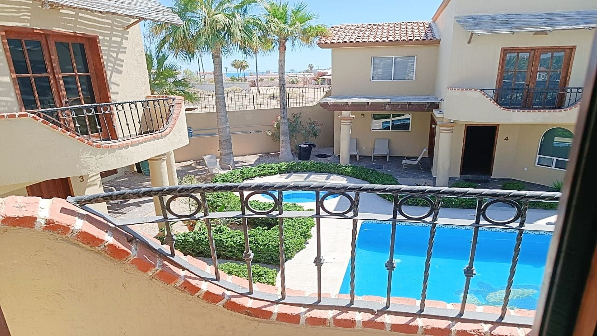 A residential area with a swimming pool, a balcony with a metal railing, and palm trees.