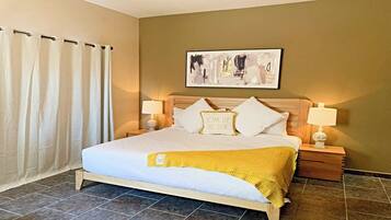 A hotel room with a bed, two bedside tables, a nightstand, a lamp, a painting on the wall, and a curtain.