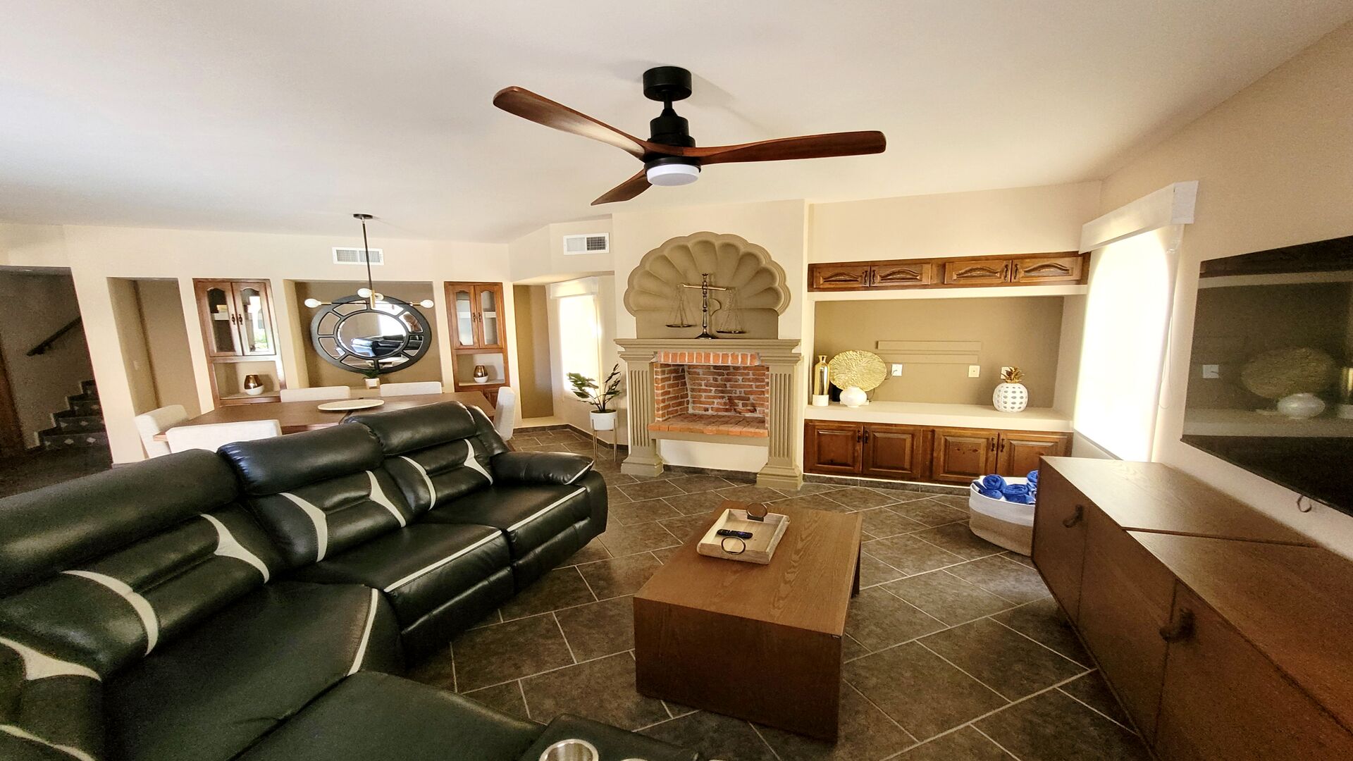 A living room with a black leather sofa, a wooden coffee table, a fireplace, and a ceiling fan.