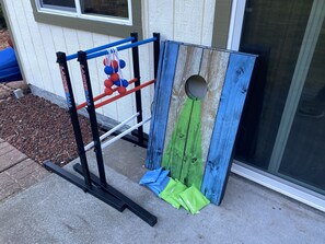 En lekställning av metall med en rutschkana och ett klätternät, placerad intill ett hus med ett fönster och en dörr.