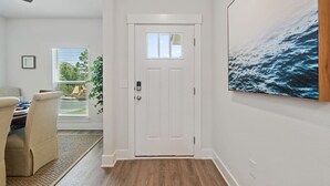 Ein Flur mit einer weißen Tür, ein Essbereich mit Tisch und Stühlen sowie ein großes Gemälde mit Meeresmotiven an der Wand.