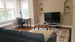 A living room with a sofa, a coffee table, a TV, and a radiator. - Comfy Bed/Free Parking&Wifi /NearHosp/ORD/MDW/DT (Berwyn)