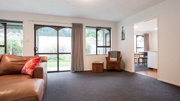 A spacious living room with a leather sofa, a small ottoman, and a chair. Large windows provide a view of the outdoors.
