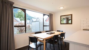 Una habitación con un ventanal grande, una mesa con sillas, un espejo y una pequeña zona de kitchenette.