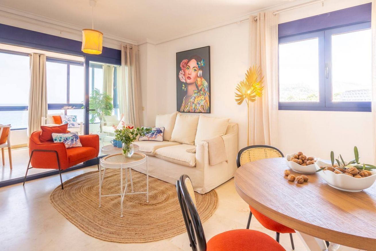 Een moderne woonkamer met een bank, een eettafel met kommen vol noten, een klein bijzettafeltje met een vaas en een schilderij aan de muur.