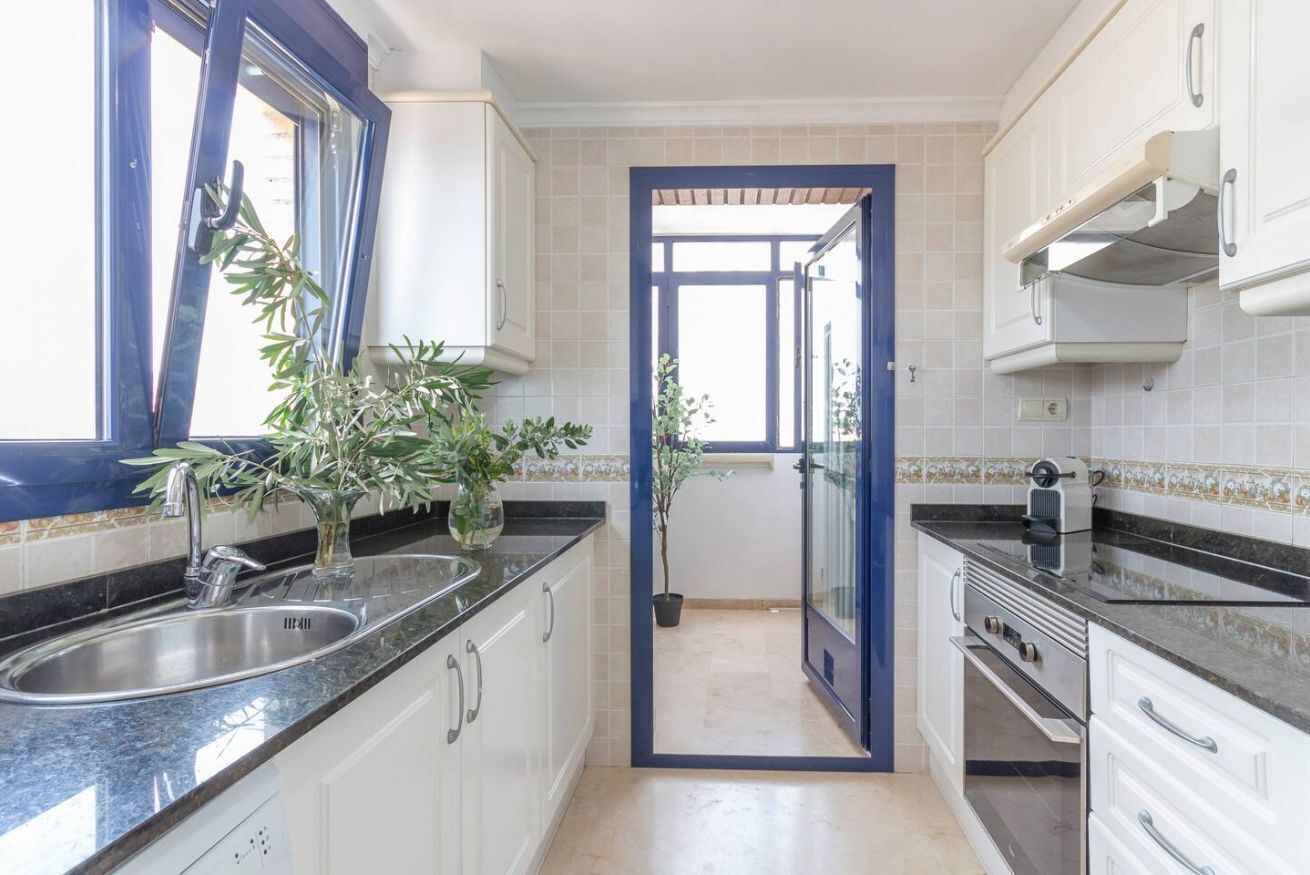 Een keuken met witte kastjes, een zwart aanrecht, een spoelbak en een oven.