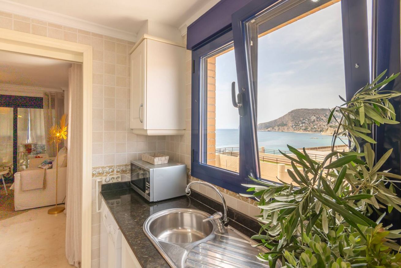 A kitchen with a view of the sea, a sink, and a toaster.