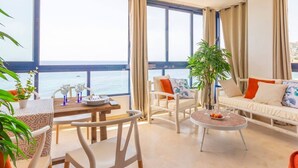 Un'ampia zona giorno con balcone vista mare, arredata con un divano, sedie e un tavolino.