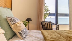 Una camera da letto con un letto, una sedia, una lampada e vista sul mare.