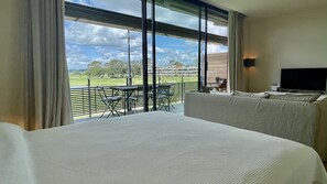 Ein Hotelzimmer mit einem großen Bett, einem Fernseher und einem Balkon mit Blick auf einen Golfplatz und Gebäude.
