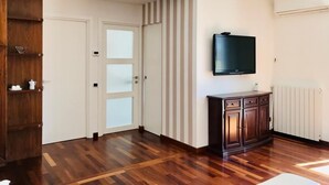 Ein Zimmer mit Holzboden, einem an der Wand montierten Fernseher, einem Schrank und einer Tür mit satinierten Glasscheiben.