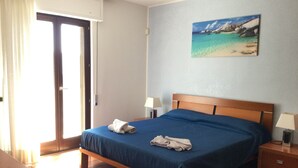 Ein Schlafzimmer mit einem hölzernen Bett, einer blauen Bettdecke und einem Bild einer Strandlandschaft an der Wand.