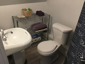 A bathroom with a white sink, a toilet, and a metal shelf unit with towels and toiletries. - Walk to the ocean, very private. Secluded, woodsy location. (Gloucester)