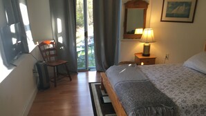A bedroom with a bed, a chair, a desk, a lamp, a mirror, and a window. - Walk to the ocean, very private. Secluded, woodsy location.  (Gloucester)