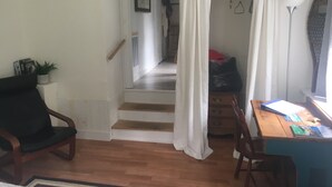 A room with a wooden floor, a desk with a computer, a chair, a staircase, and a door with white curtains. - Walk to the ocean, very private. Secluded, woodsy location.  (Gloucester)