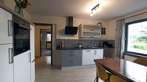 Eine moderne Küche mit Einbauofen, Mikrowelle und einem Flachbildfernseher. Es gibt einen Essbereich mit einem Holztisch und gelben Stühlen.