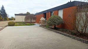 Ein Gebäude mit gepflasterter Auffahrt, Backsteinmauern und einem kleinen Garten mit Sträuchern und einem Baum.