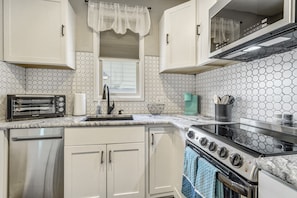 A kitchen with white cabinets, a stainless steel refrigerator, a black stove, and a microwave.