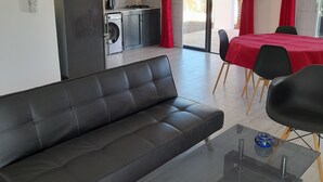 Ett modernt vardagsrum med en svart lädersoffa, ett soffbord i glas och en matplats med en röd duk.
