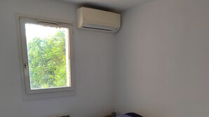 A bedroom with a bed, a window, a radiator, and an air conditioning unit. - 0000000000 (rognes)