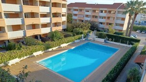 A rectangular swimming pool surrounded by a paved deck, with white lounge chairs and a small poolside table. - 0000000000 (rognes)
