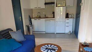 A modern living room with a blue sofa, a round wooden coffee table, and a kitchen in the background. - 0000000000 (rognes)