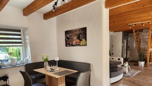 A modern living room with a wooden ceiling, a black leather sofa, a wooden coffee table, and a dining area with a small table and chairs.