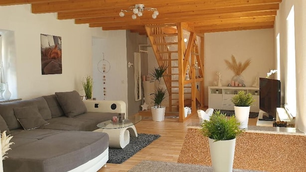 A modern living room with a grey sofa, a glass coffee table, and a wooden staircase leading to another room.