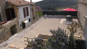 A courtyard with a gravel ground, a red umbrella, and a table with chairs. - Escape To Umbria, Little Alley (Porchiano del Monte)