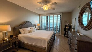 A bedroom with a bed, a ceiling fan, a nightstand with a lamp, a dresser, and a large mirror. - Eden Condominium W 1104 Gulf Front Condo with Stunning Views! (Pensacola)