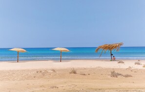 A beach with three straw umbrellas and a thatched structure.