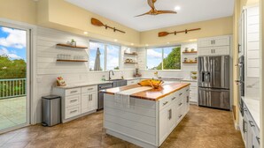 A modern kitchen with a large island, white cabinetry, and a stainless steel refrigerator. - Paradise Found (Waikoloa Village)