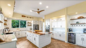 A spacious kitchen with white cabinetry, a large island, and a ceiling fan. - Paradise Found (Waikoloa Village)