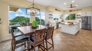A spacious kitchen with a central island, large windows, and a view of greenery. - Paradise Found (Waikoloa Village)