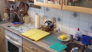 A kitchen with wooden cabinets, a countertop with various items, a kettle, a rolling pin, and a window with a view of the outside. - Carpe Diem Frankenthal Palatinate Wine Route Kurpfalz (Frankenthal)
