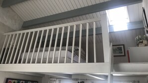 Huone, jossa on valkoinen parvekeraita, paljaat kattopalkit ja ikkuna, josta pääsee sisään luonnonvaloa.