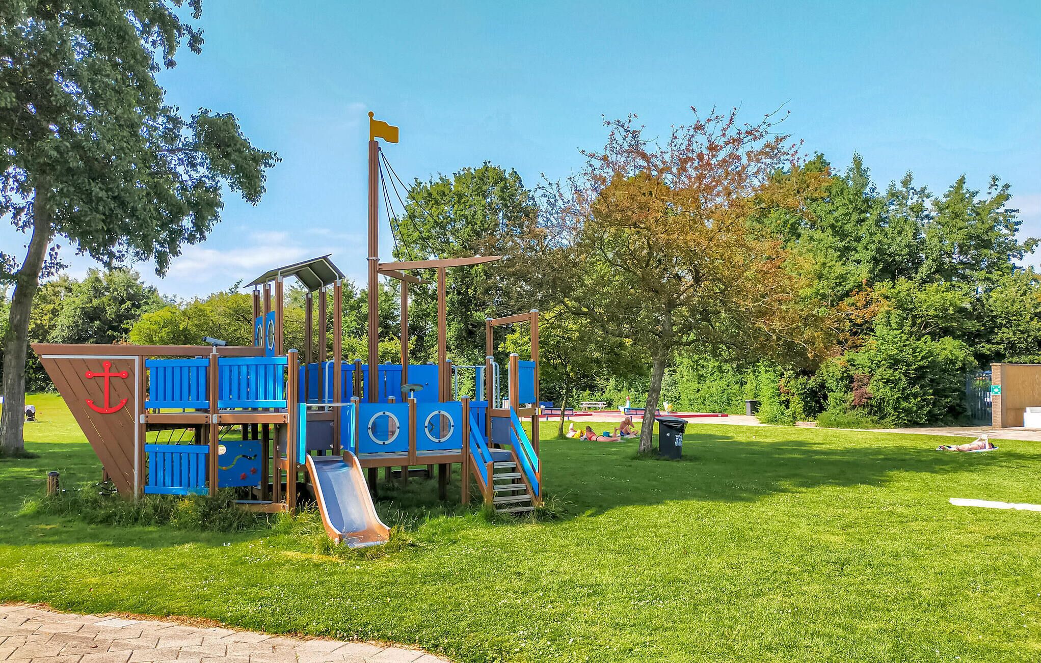 Une aire de jeux avec un toboggan, des structures d’escalade et un mât pour drapeau.