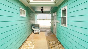 Un porche abrité avec un revêtement de façade de couleur turquoise, un ventilateur de plafond et deux chaises.