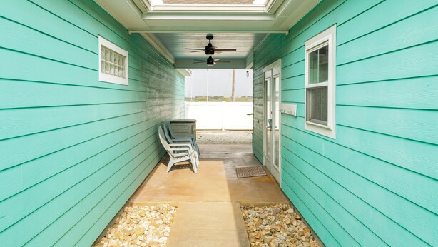 A covered porch with teal siding, a ceiling fan, and two chairs.