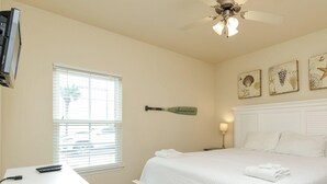 A bedroom with a bed, a desk, a ceiling fan, and a window with blinds.