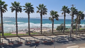 A beach with palm trees, a view of the ocean, and a pedestrian walkway. - Masarik Apartments (Bat Yam)