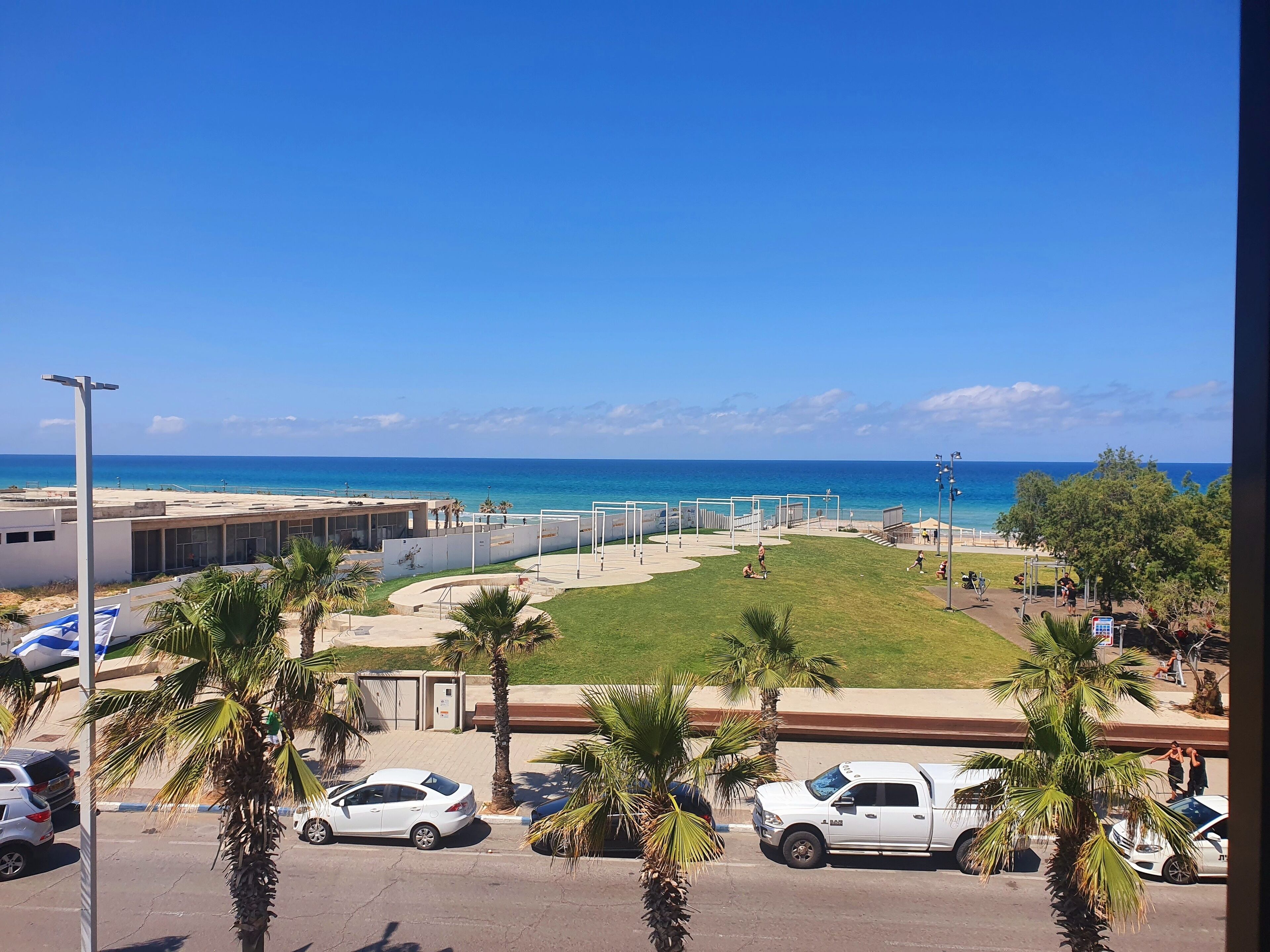 Un aparcamiento con coches blancos, palmeras y vistas al océano.
