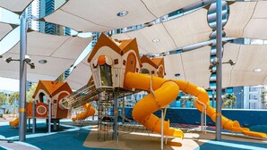 A playground with a climbing structure, slides, and a netted area. - Masarik Apartments (Bat Yam)