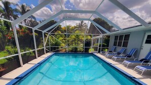 Une piscine d’un bleu éclatant, surmontée d’une structure blanche, entourée de chaises longues et offrant une vue sur un jardin.