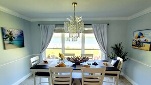 Un coin repas avec une table dressée pour quatre personnes, des chaises blanches, un lustre et des œuvres d’art accrochées aux murs.